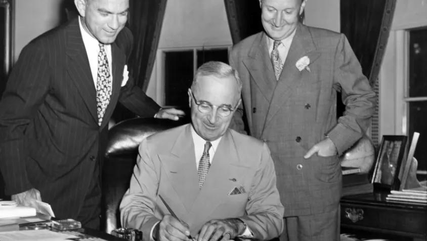 President Truman signs a bill while two men look on